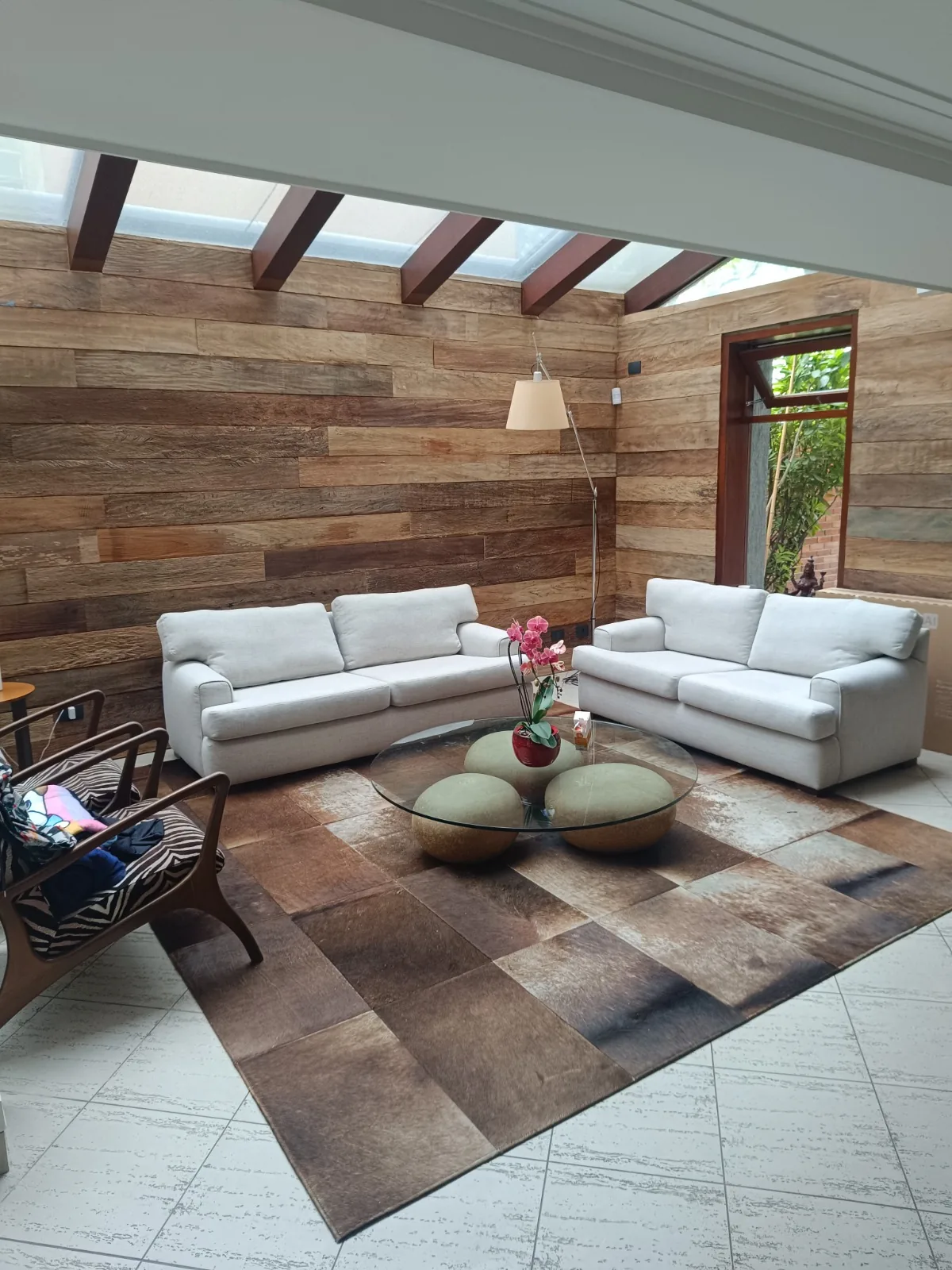 Sala com teto de madeira, sofás brancos e tapete de couro